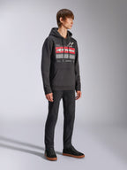Sweat à capuche Harken Alpinestars, sweat à capuche noir en polaire, doté d'un grand graphisme sur la poitrine avec lettrage Alpinestars rouge et logo étoile, poche kangourou, porté par un mannequin avec un pantalon et des baskets noirs, style streetwear décontracté motorsport
