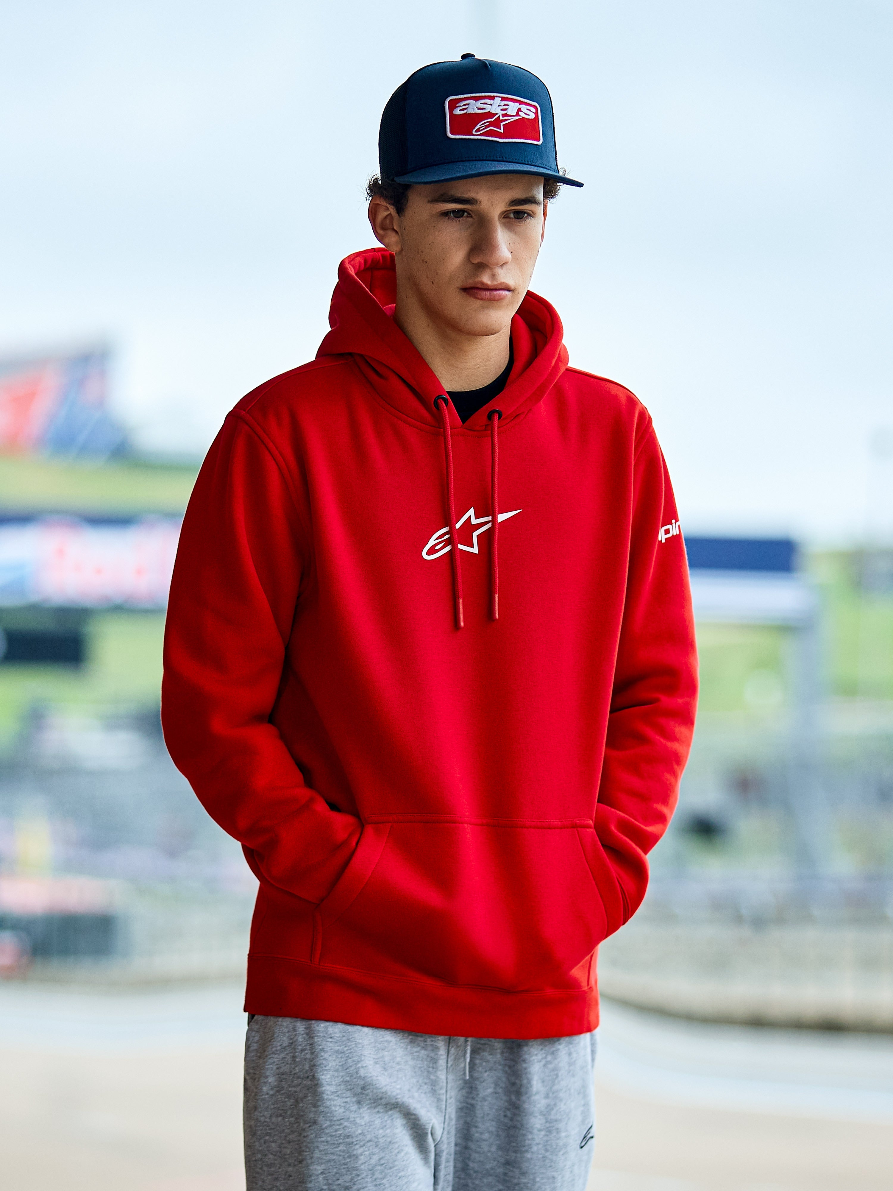 Sweat à capuche Alpinestars Frontal, hoodie en polaire rouge avec logo Astars blanc sur la poitrine, poche kangourou et capuche à cordon de serrage, porté par un homme avec une casquette bleue, style streetwear décontracté motorsport