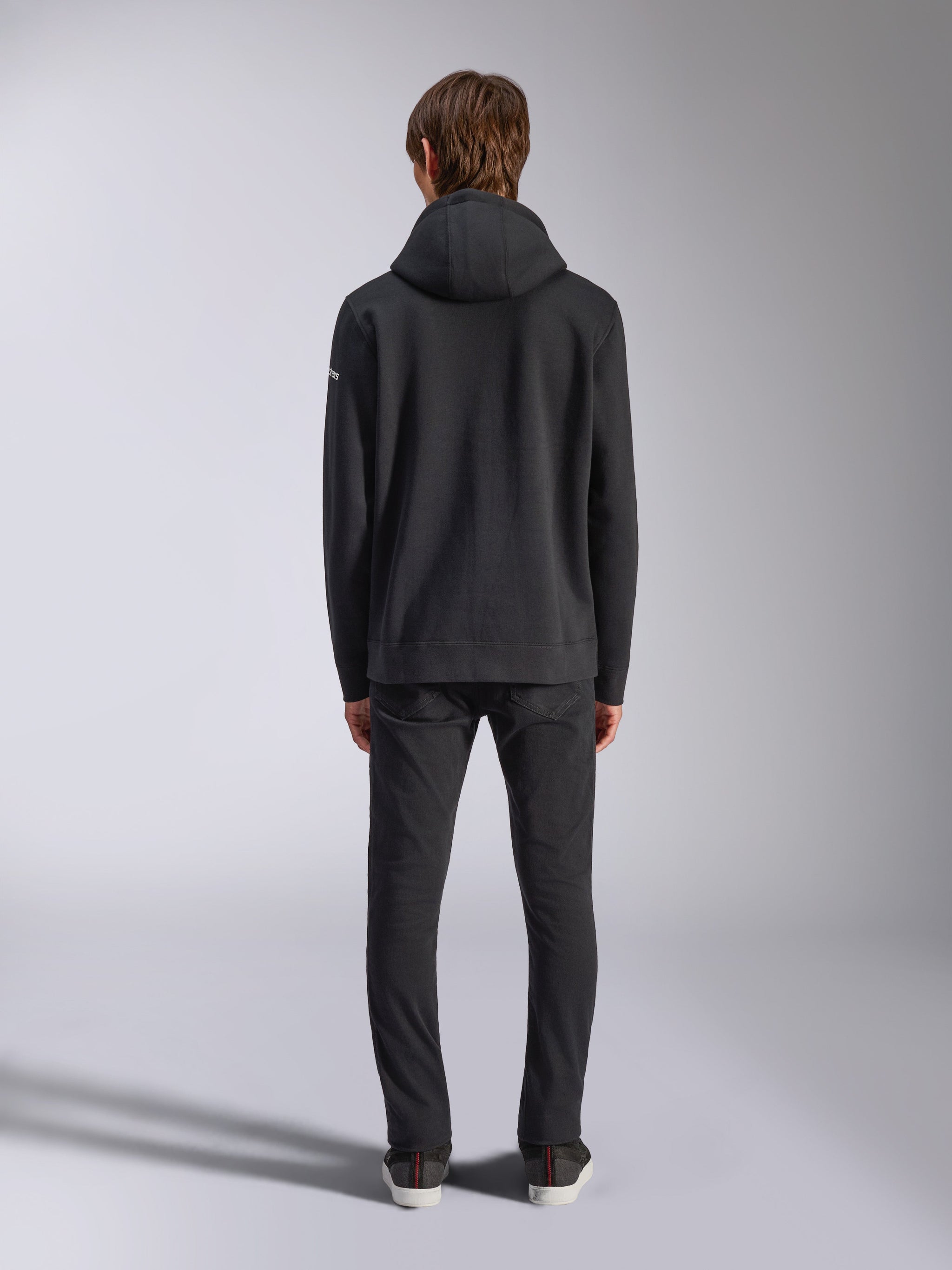 Alpinestars Frontal Hoodie, streetwear décontracté, noir, vue arrière d'un mannequin portant un sweat à capuche en polaire à enfiler, doté d'un ourlet et de poignets côtelés, petit logo wordmark blanc sur la manche, associé à un pantalon noir