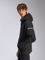 Sweat à capuche Frontal Alpinestars, polaire noire à enfiler, mannequin de profil, logo Alpinestars blanc sur la manche, poche kangourou, streetwear décontracté d'inspiration sport automobile