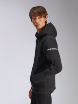 Sweat à capuche Frontal Alpinestars, polaire noire à enfiler, mannequin de profil, logo Alpinestars blanc sur la manche, poche kangourou, streetwear décontracté d'inspiration sport automobile