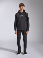 Sweat à capuche Alpinestars Frontal, sweat à capuche noir en polaire, logo Alpinestars blanc sur la poitrine et la manche, poche kangourou, capuche à cordon de serrage, porté avec un pantalon noir, design décontracté inspiré des sports mécaniques