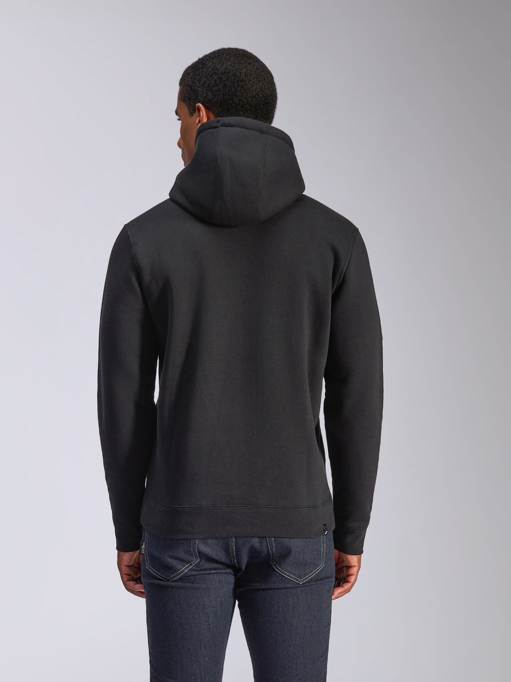 Alpinestars Blaze V3 Hoodie, vue arrière d'un sweat à capuche noir en polaire, style streetwear décontracté, avec poignets et ourlet côtelés, capuche doublée en jersey, porté avec un jean bleu foncé