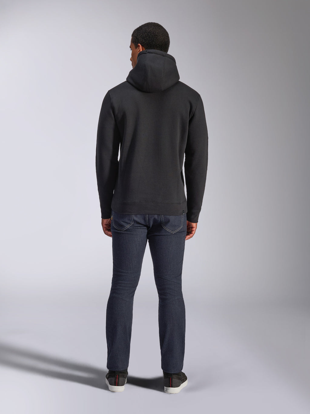 Sweat à capuche Alpinestars Blaze V3, style streetwear décontracté, noir, vue de dos d'un sweat à capuche en polaire, porté avec un jean denim bleu foncé et des chaussures noires, design épuré inspiré des sports mécaniques