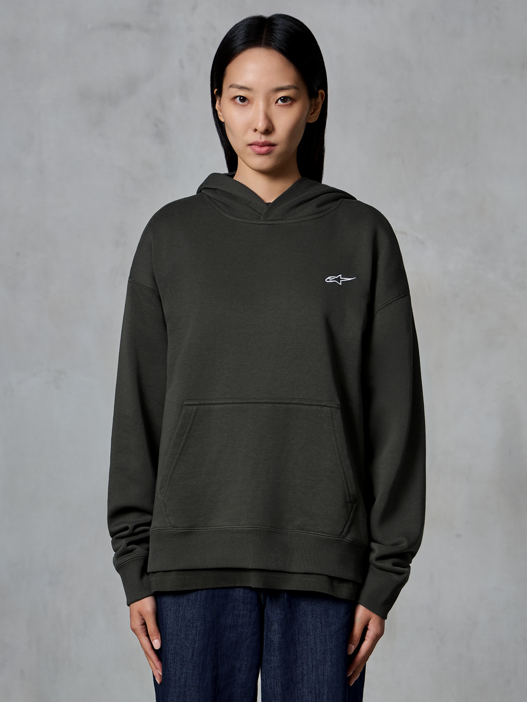 Sweat à capuche Alpinestars Essentials Ageless, Off Black, porté par un mannequin, arborant un petit logo Astars blanc sur la poitrine, poche kangourou à l'avant, finition délavée à la pierre, streetwear décontracté en molleton de qualité supérieure