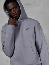 Sweat à capuche Alpinestars Essentials Ageless, Silver, mannequin portant le sweat avec la capuche relevée, petit logo Alpinestars noir sur la poitrine, poche kangourou, poignets côtelés, style streetwear décontracté