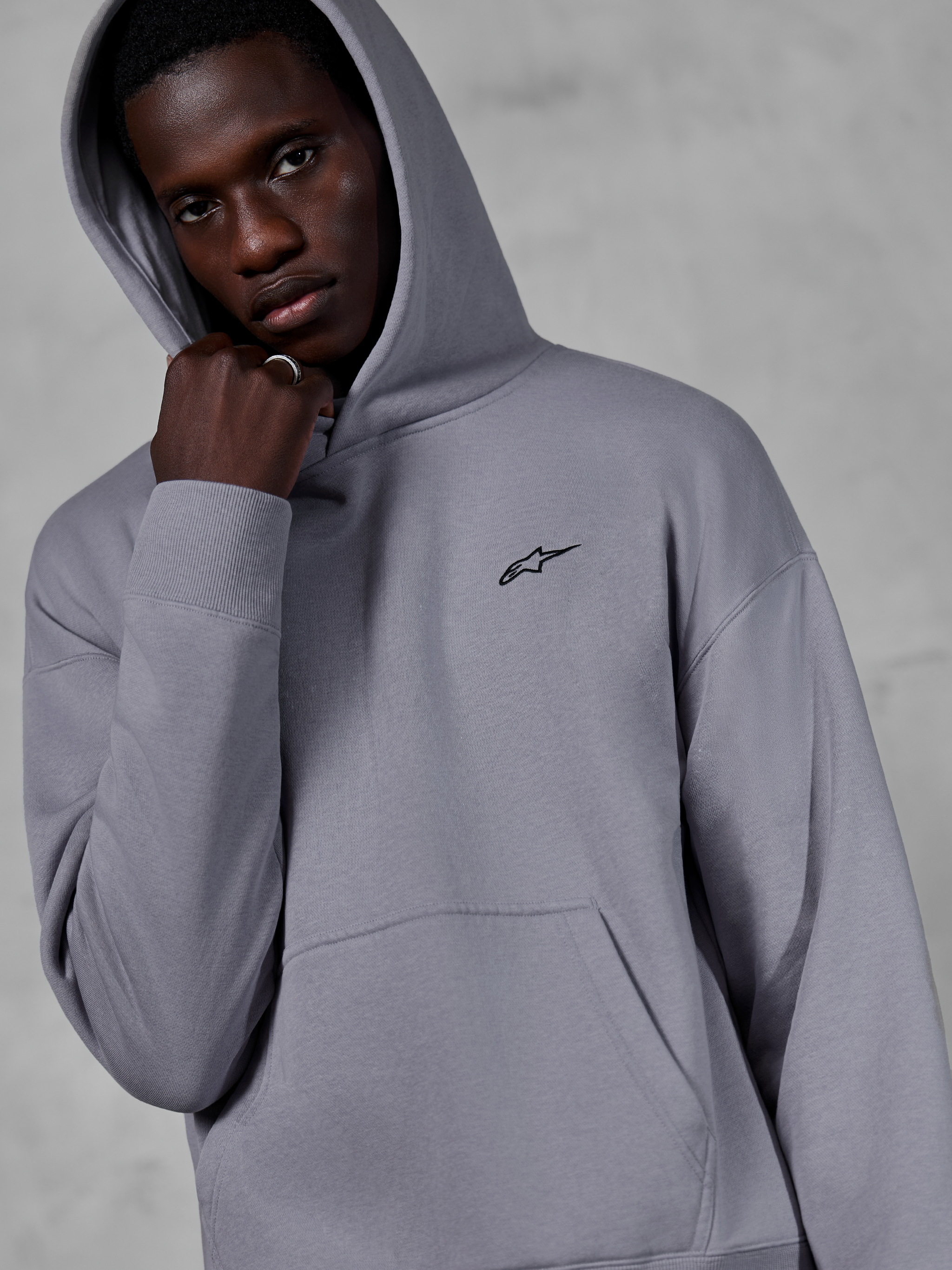 Sweat à capuche Alpinestars Essentials Ageless, Silver, mannequin portant le sweat avec la capuche relevée, petit logo Alpinestars noir sur la poitrine, poche kangourou, poignets côtelés, style streetwear décontracté