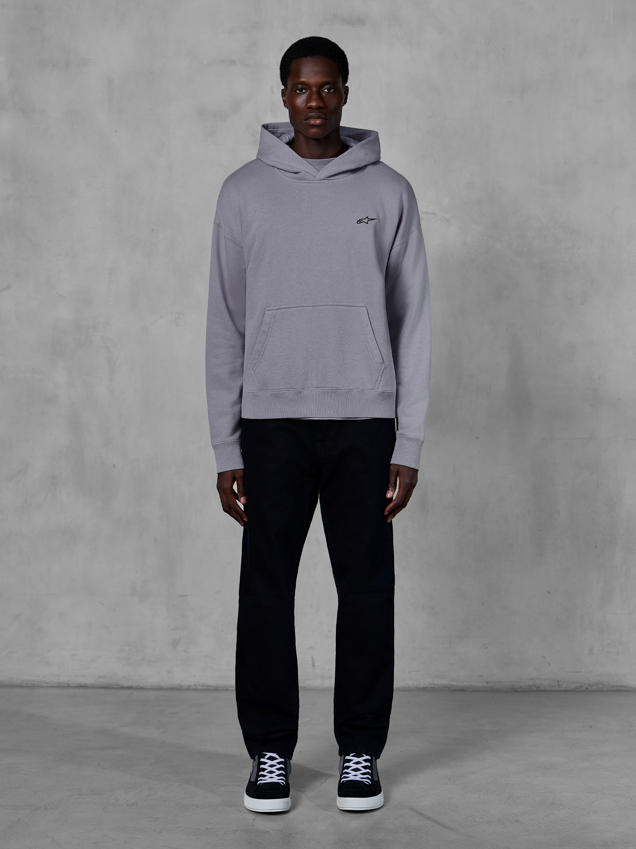 Alpinestars Essentials Ageless Hoodie, Argent, mannequin homme portant un style streetwear décontracté, petit logo Alpinestars noir sur la poitrine, poche kangourou à l'avant, design minimaliste, associé à un pantalon noir et des baskets.