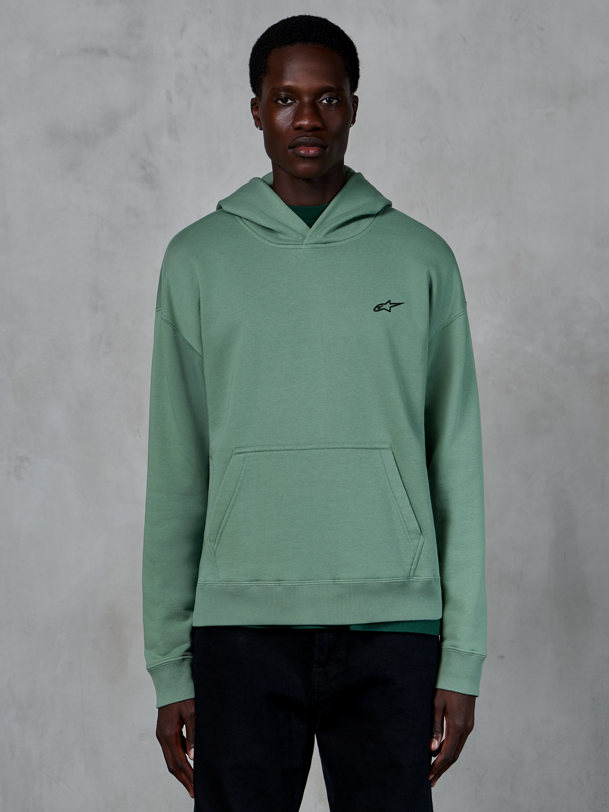Sweat à capuche Alpinestars Essentials Ageless, vert cactus, sweat à capuche décontracté en molleton avec finition lavage à la pierre, doté d'un petit logo étoile noir sur la poitrine et d'une poche kangourou à l'avant, porté par un mannequin dans un cadre lifestyle épuré
