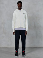 Alpinestars Essentials Ageless Zip Hoodie, sweat à capuche zippé blanc cassé, coupe décontractée avec petit logo noir sur la poitrine, porté avec un pantalon de jogging noir et des baskets, style streetwear décontracté inspiré du sport automobile