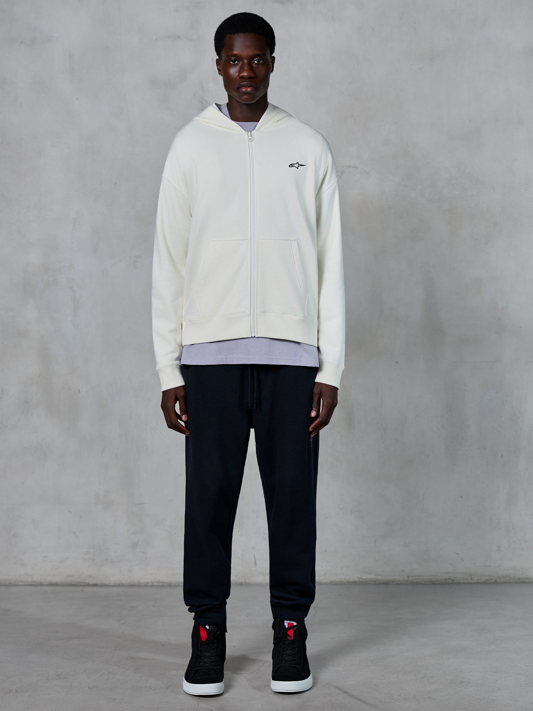 Alpinestars Essentials Ageless Zip Hoodie, Off White full-zip hoodie, relaxed fit with small black logo on chest, worn with black sweatpants and sneakers, casual motorsport-inspired streetwear.