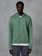Sweat à capuche zippé Alpinestars Essentials Ageless, vêtement streetwear décontracté, vert Cactus, avec un logo brodé discret sur la poitrine, des poches kangourou divisées et des poignets côtelés, porté par un mannequin homme sur un fond gris texturé