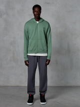 Sweat à capuche zippé Alpinestars Essentials Ageless, sweat à capuche zippé, vert cactus, porté par un mannequin avec un jogging gris foncé et des baskets noires, arborant un petit logo Alpinestars noir sur la poitrine, coupe décontractée, style streetwear décontracté