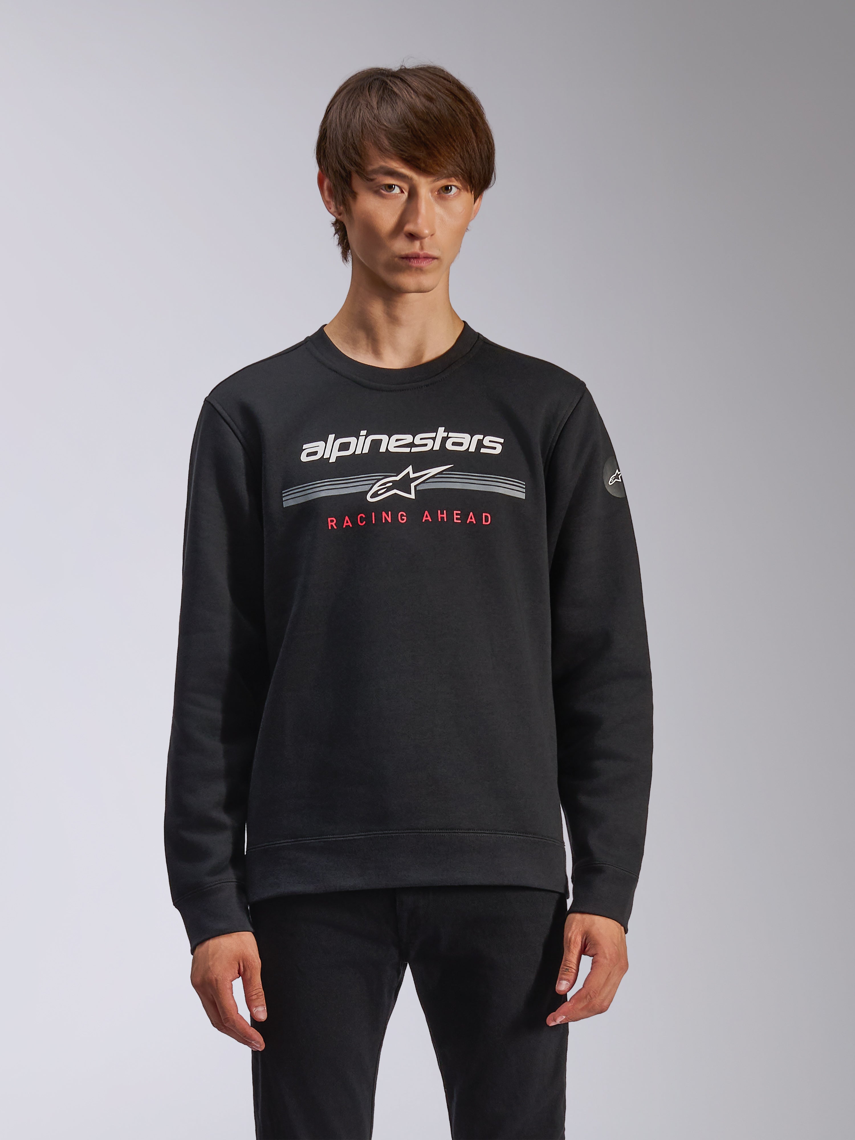 Alpinestars Bettern Crew, sweatshirt à col rond, noir, avec marquage Alpinestars blanc, rayures horizontales grises et texte rouge 'RACING AHEAD', style streetwear décontracté inspiré du sport automobile