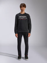 Alpinestars Bettern Crew, Black Crew Neck Sweatshirt, features white alpinestars logo with grey horizontal stripes and red 'RACING AHEAD' text, casual motorsport streetwear, worn by model with black pants and sneakers