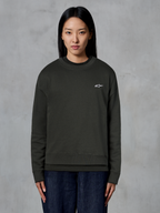 Alpinestars Essentials Ageless Crew, sweat-shirt à col rond de qualité supérieure, Off Black, avec un petit logo Alpinestars blanc sur la poitrine, style streetwear décontracté porté par un mannequin avec un jean foncé