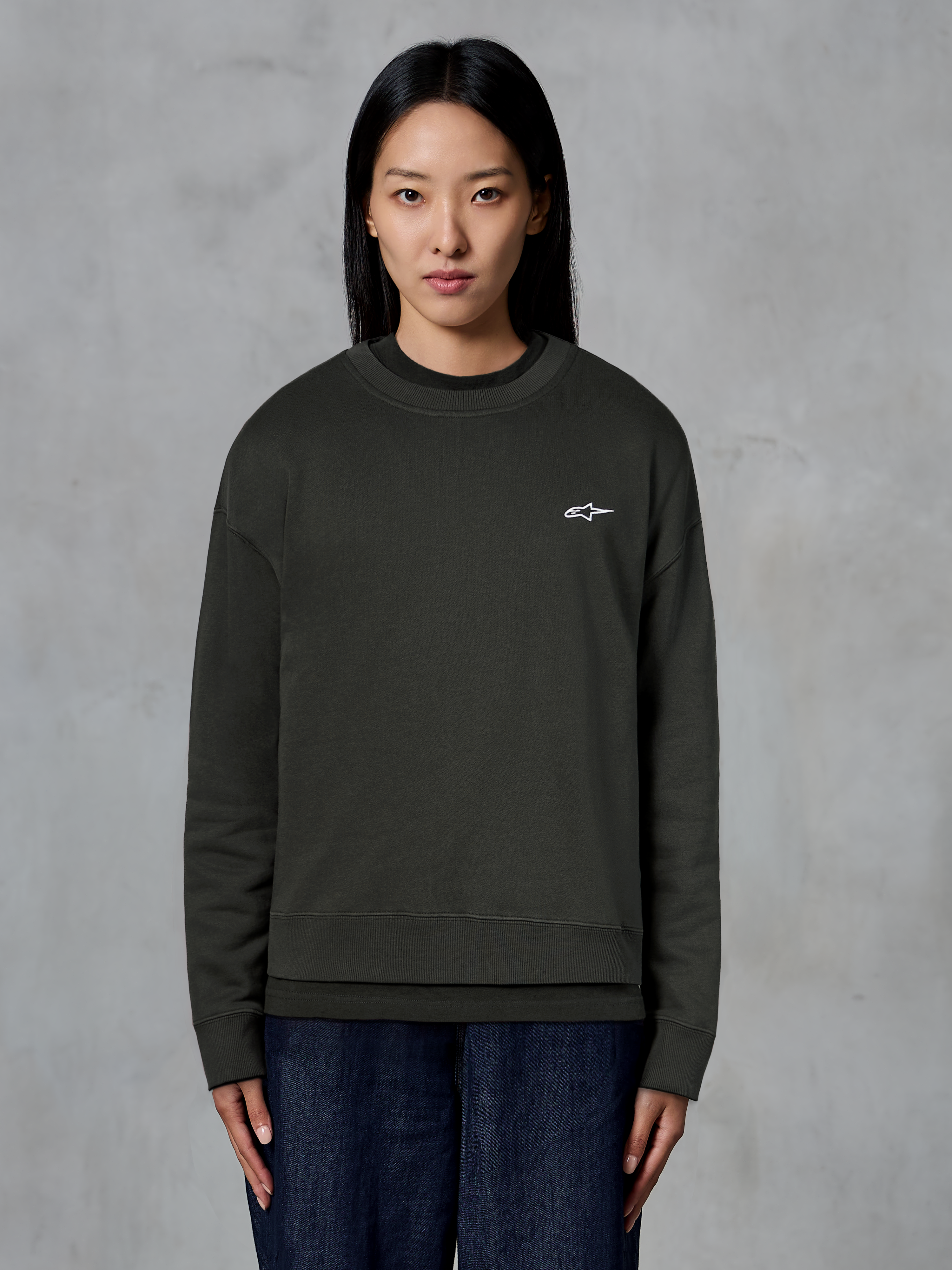 Alpinestars Essentials Ageless Crew, sweat-shirt à col rond de qualité supérieure, Off Black, avec un petit logo Alpinestars blanc sur la poitrine, style streetwear décontracté porté par un mannequin avec un jean foncé