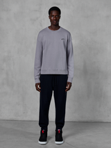 Alpinestars Essentials Ageless Crew, sweat-shirt à col rond argenté, porté par un mannequin avec un jogging noir et des baskets noires, arborant un petit logo Alpinestars noir sur la poitrine, streetwear décontracté inspiré du sport automobile