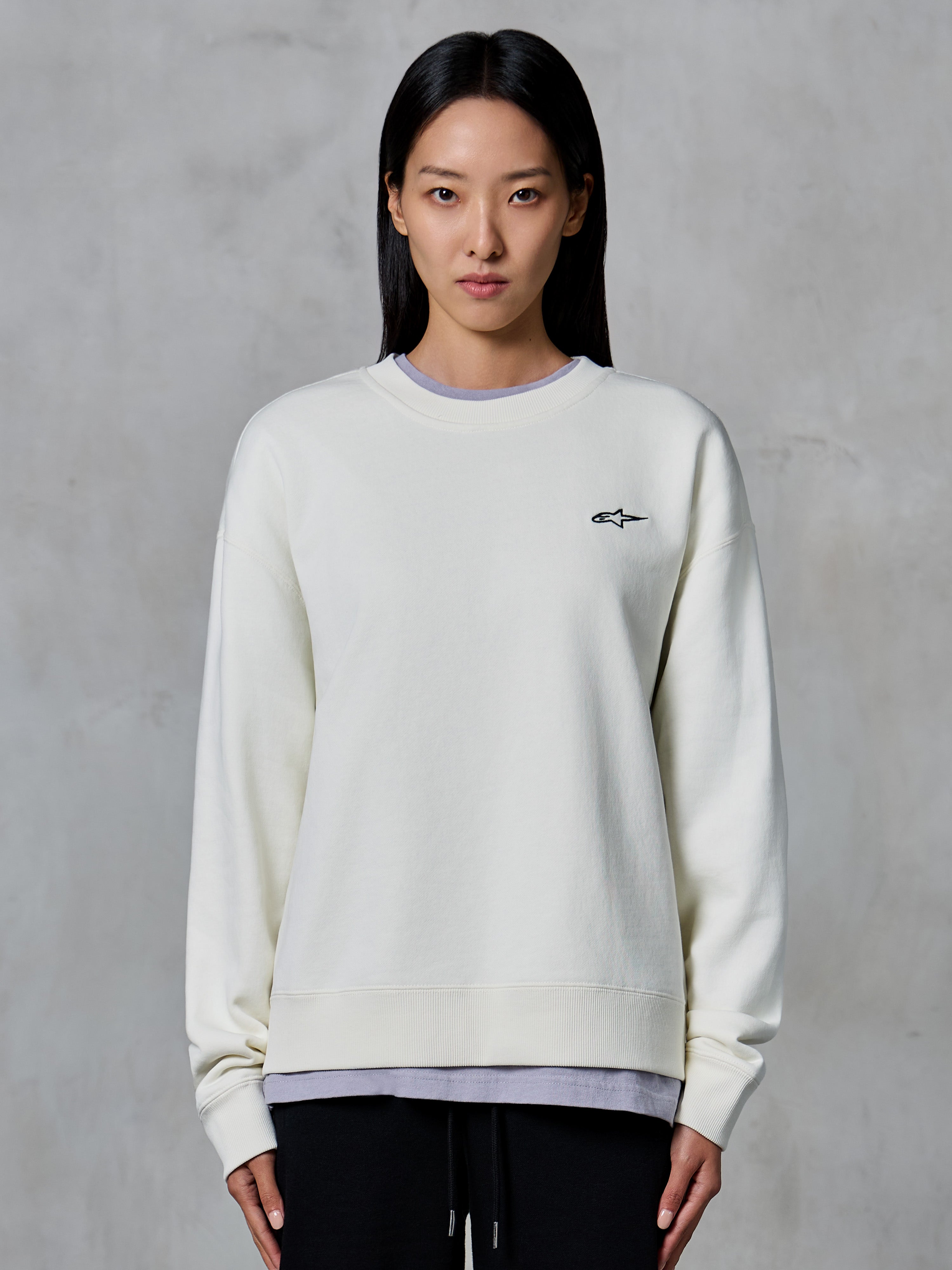 Alpinestars Essentials Ageless Crew, sweat-shirt à col rond, blanc cassé, avec un petit logo Alpinestars noir sur la poitrine, vêtement lifestyle décontracté porté par une femme