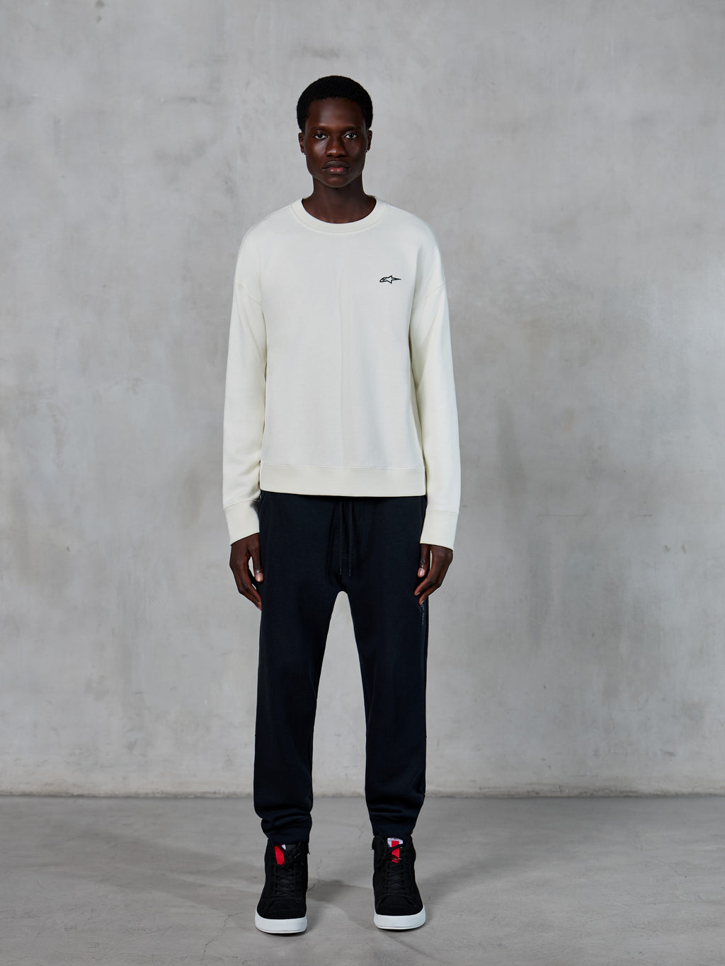 Alpinestars Essentials Ageless Crew, sweat-shirt à col rond, blanc cassé avec petit logo étoile noir, porté par un mannequin avec un jogging noir, streetwear décontracté d'inspiration sport mécanique