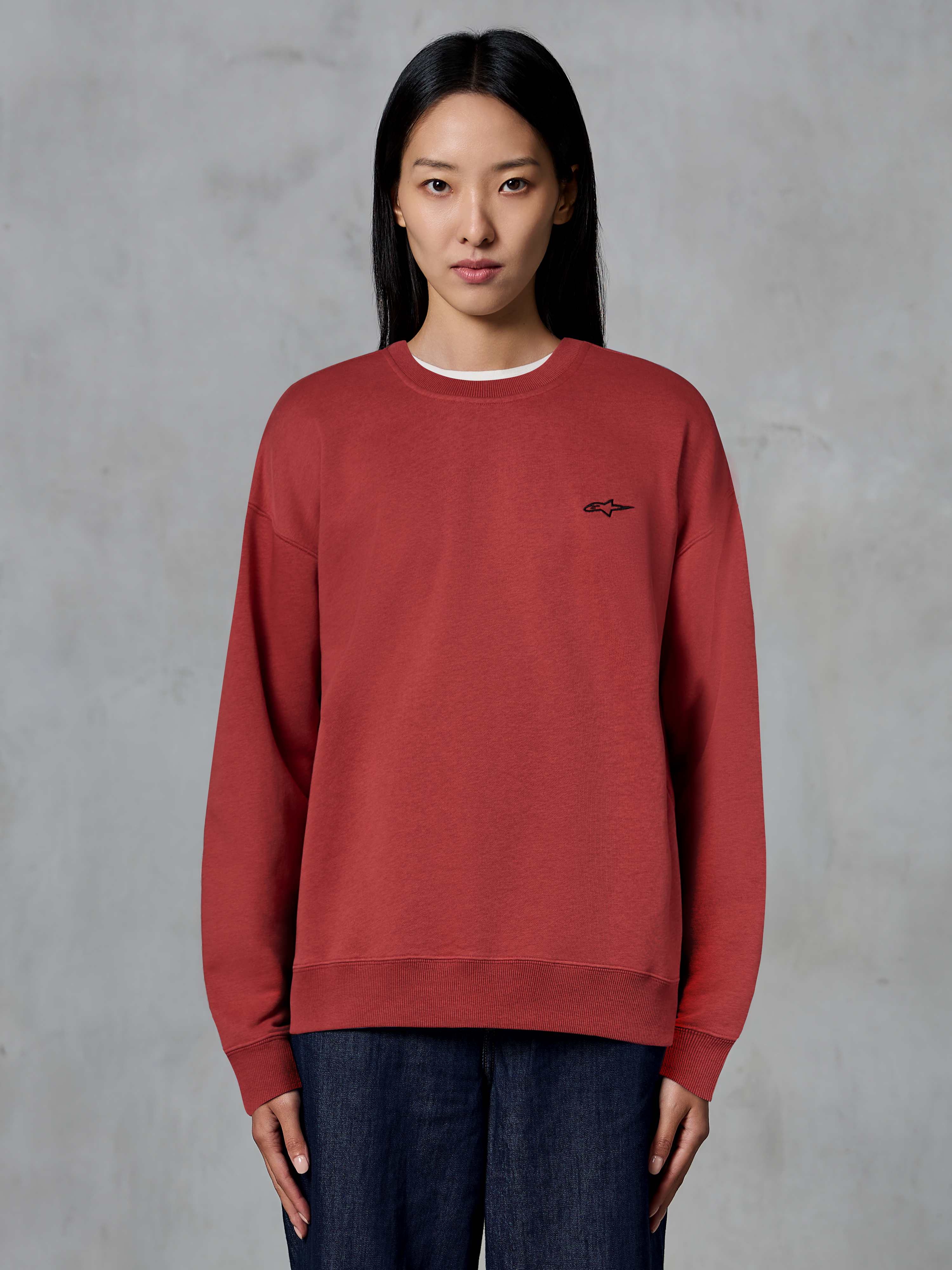 Alpinestars Essentials Ageless Crew, sweat-shirt à col rond rouge brique, petit logo noir sur la poitrine, polaire de qualité supérieure, porté par un mannequin, streetwear décontracté inspiré du sport automobile