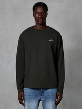 Alpinestars Essentials Ageless LS Tee, t-shirt à manches longues, noir, avec un petit logo Alpinestars blanc sur la poitrine, porté par un mannequin avec un jean bleu, streetwear décontracté en coton biologique