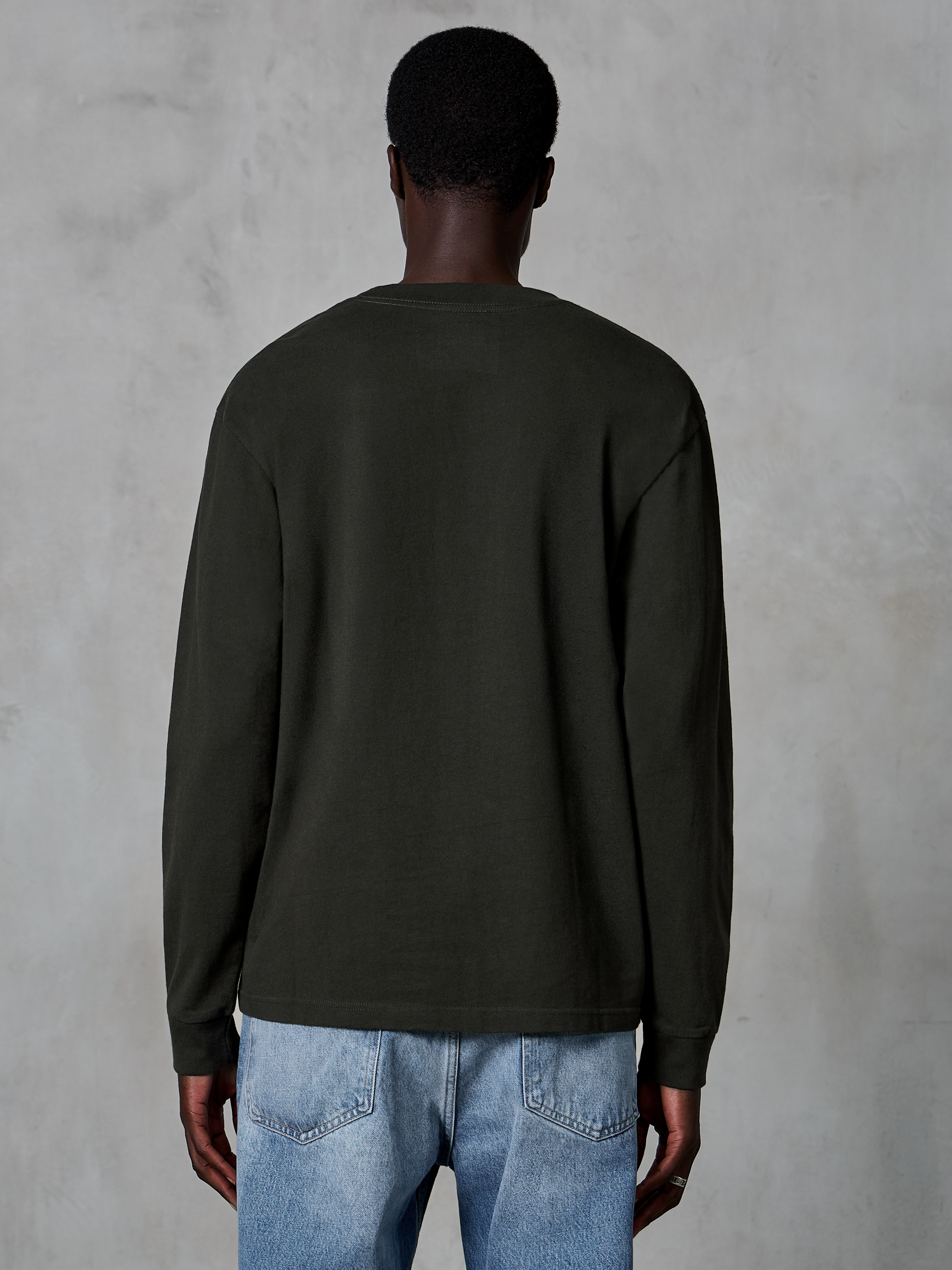 Alpinestars Essentials Ageless LS Tee, t-shirt à manches longues, noir, vue arrière montrant un design épuré et une coupe décontractée, porté par un mannequin avec un jean bleu, streetwear décontracté inspiré du sport automobile