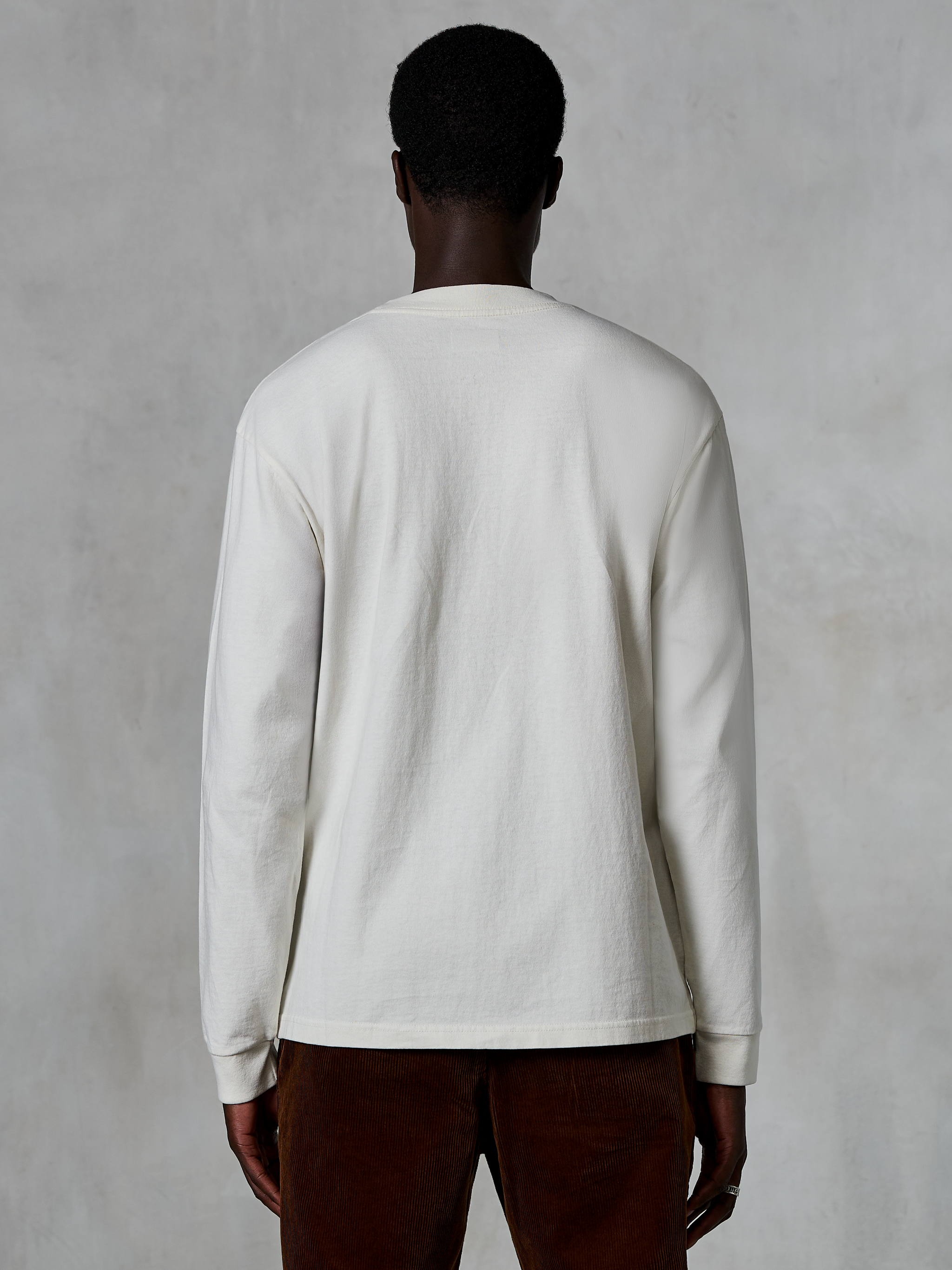 Alpinestars Essentials Ageless LS Tee, Long-Sleeve T-Shirt, Off White, back view of a person wearing the shirt with brown corduroy pants, relaxed fit, textured organic cotton fabric, minimalist casual streetwear