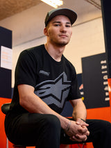 Alpinestars Fasting CSF Tee, t-shirt à manches courtes, noir, grand logo étoile géométrique gris avec le texte Forward Innovation, porté par un homme dans un cadre de sport automobile décontracté, vêtements de sport lifestyle