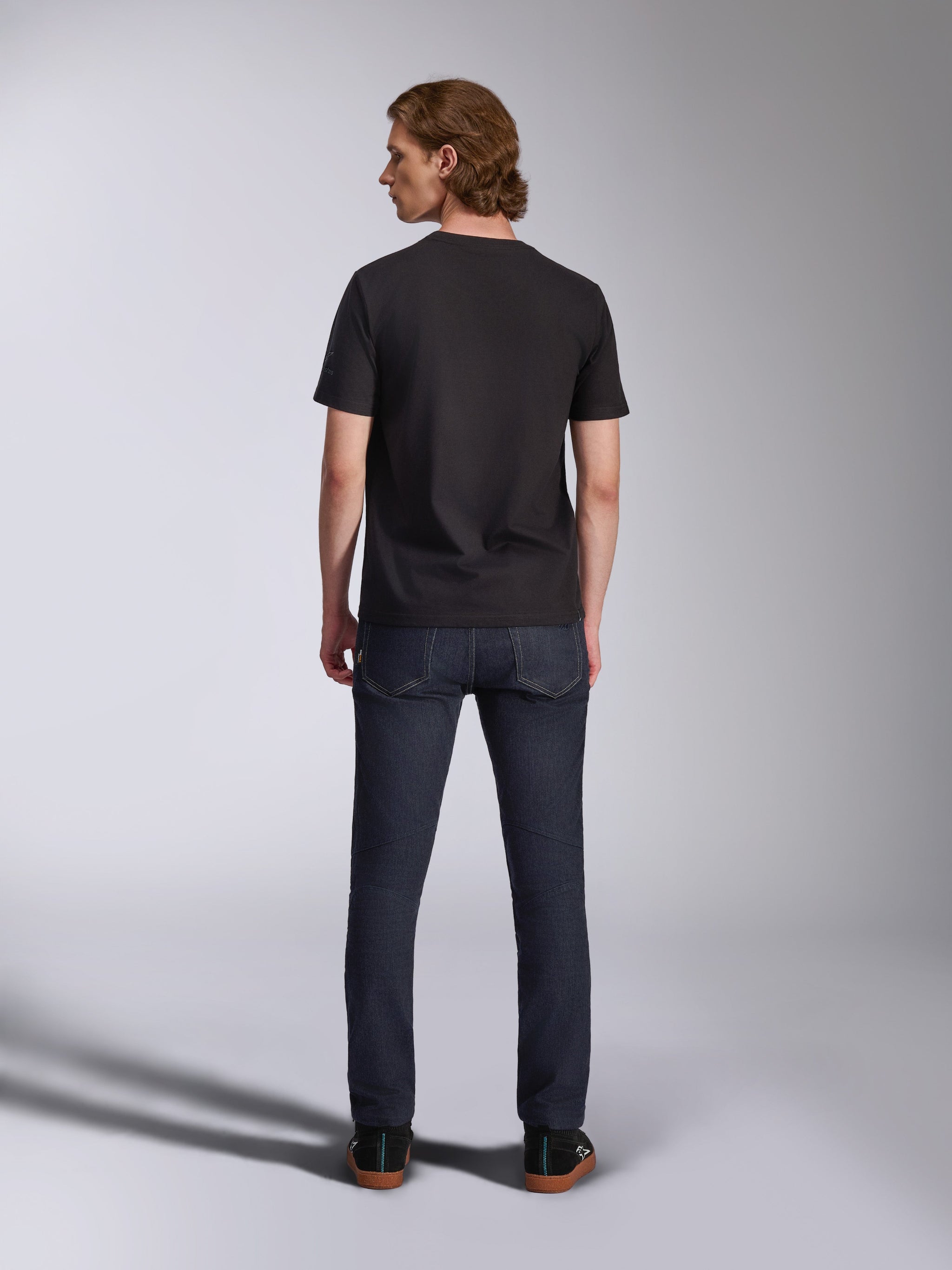 T-shirt Global CSF Alpinestars, t-shirt à manches courtes noir, vue de dos d'un mannequin homme portant le t-shirt avec un jean en denim foncé, streetwear décontracté inspiré du sport automobile