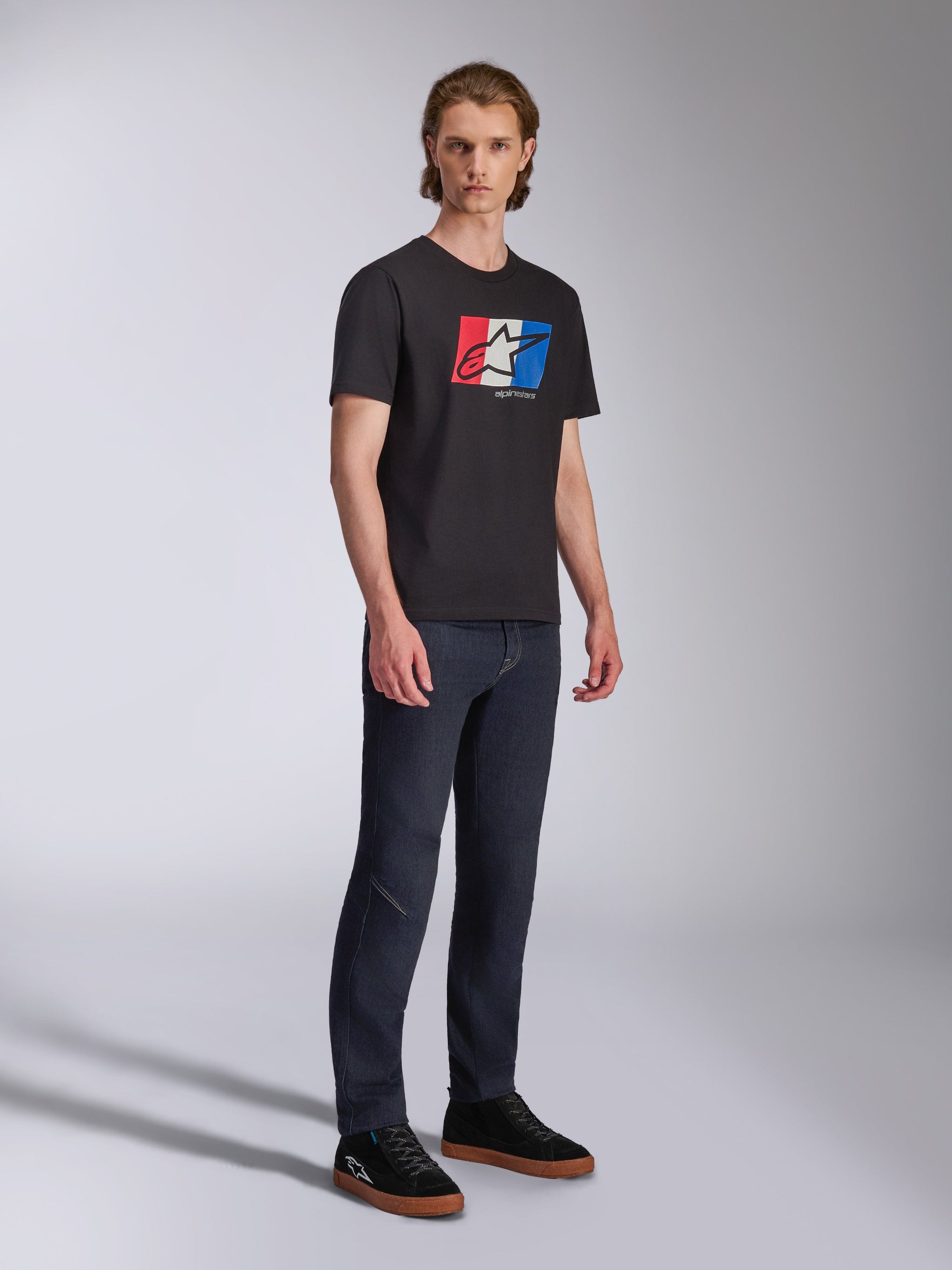 Alpinestars Global CSF Tee, t-shirt à manches courtes, noir avec graphique de logo rouge, blanc et bleu, streetwear motorsport décontracté, photo en pied d'un mannequin portant un jean foncé et des baskets noires