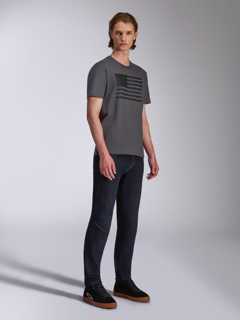 Alpinestars Waving CSF Tee, Short Sleeve T-Shirt, Charcoal, Black Waving Flag Graphic, worn by a model with dark jeans and sneakers, Casual Motorsport Streetwear