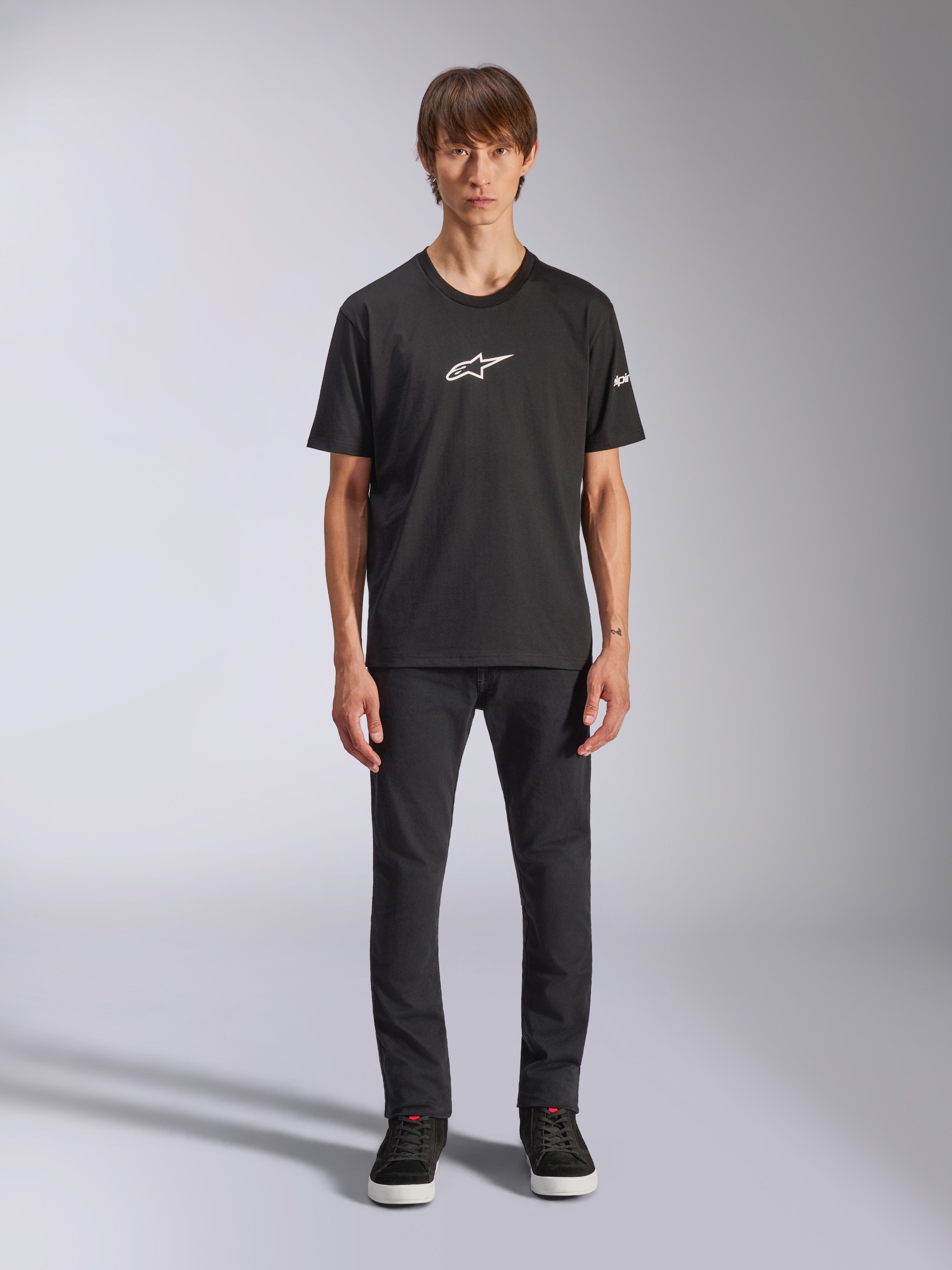 T-shirt Alpinestars Frontal CSF, T-shirt à manches courtes, noir, logo Alpinestars blanc sur la poitrine, porté par un mannequin avec un pantalon noir et des chaussures noires, vêtement de sport performant et décontracté