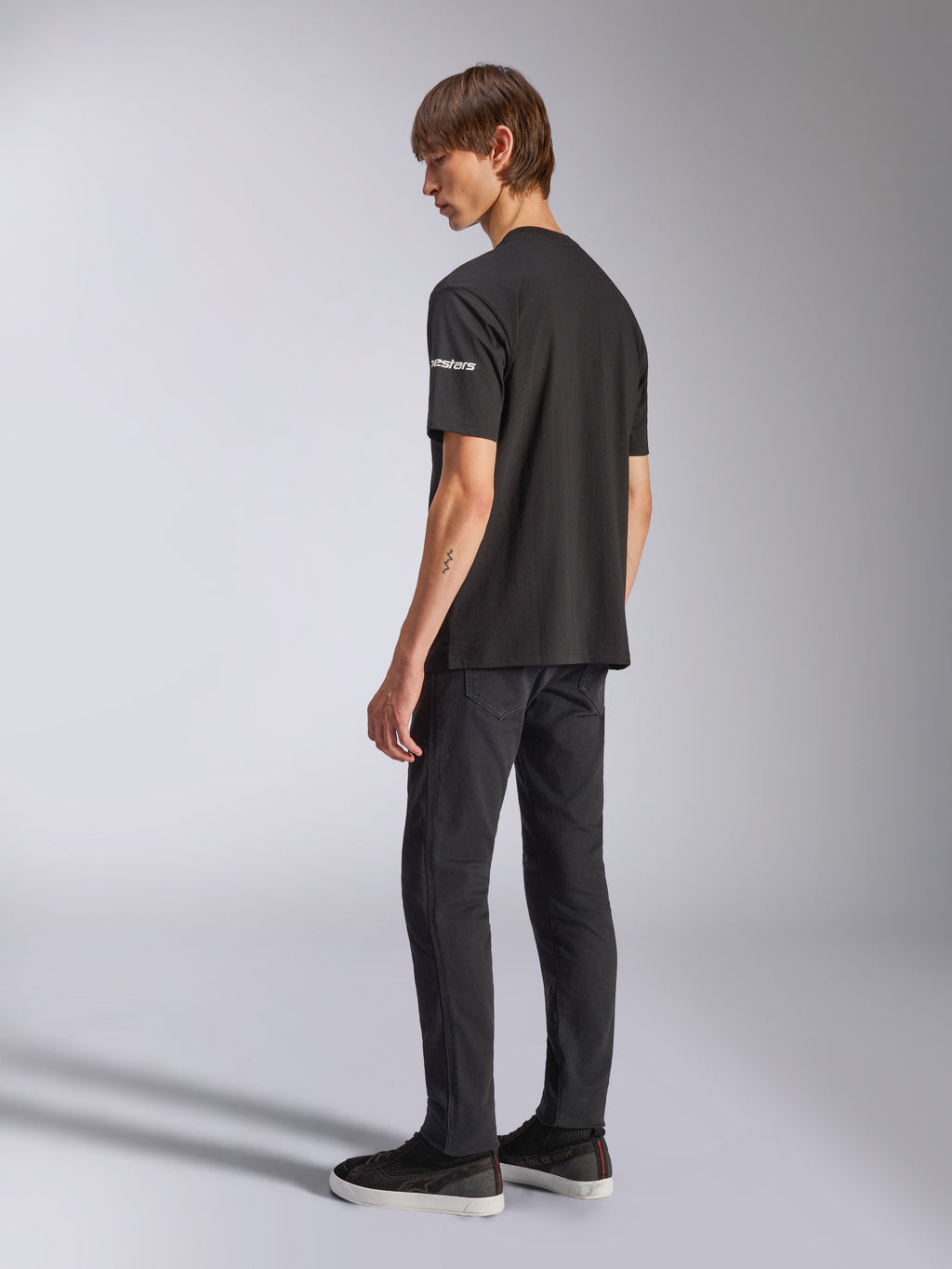 T-shirt Alpinestars Frontal CSF, t-shirt à manches courtes, noir, marquage astars blanc sur la manche, porté par un mannequin avec un pantalon et des chaussures noirs, design décontracté inspiré du sport automobile