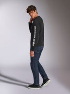 T-shirt Alpinestars Trackside CSF à manches longues, noir avec inscription Alpinestars blanche verticale sur la manche, porté par un mannequin avec un jean foncé et des baskets, vêtements de sport décontractés d'inspiration sport mécanique
