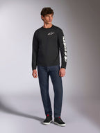 Alpinestars Trackside CSF Tee, t-shirt à manches longues, noir et blanc, porté avec un jean bleu foncé et des baskets noires, arborant le logo Ride 4.0 blanc sur la poitrine et le lettrage Alpinestars sur la manche, streetwear décontracté inspiré des sports mécaniques