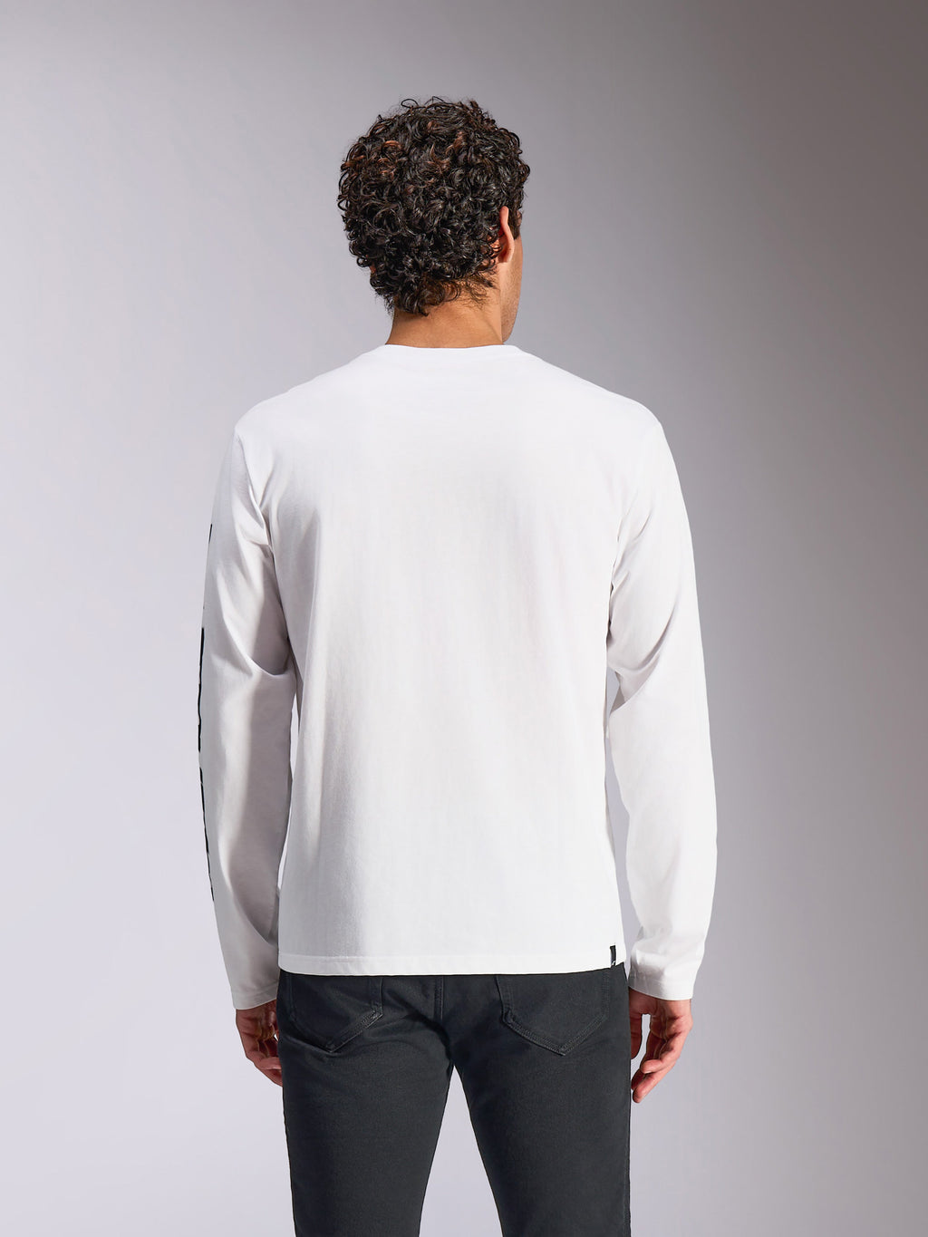 T-shirt à manches longues Alpinestars Trackside CSF, blanc, vue de dos sur mannequin, associé à un pantalon noir, tissu blanc épuré, style streetwear décontracté inspiré des sports mécaniques