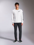 T-shirt à manches longues Alpinestars Trackside CSF, blanc avec logos noirs, petit logo sur la poitrine et texte vertical sur la manche, porté par un mannequin avec un pantalon sombre et des baskets noires, streetwear décontracté inspiré du sport automobile