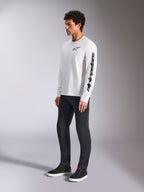Alpinestars Trackside CSF Tee, t-shirt à manches longues, blanc, logo étoile noir sur la poitrine et logo textuel sur la manche gauche, porté par un mannequin homme avec un pantalon sombre et des baskets, style sportswear décontracté
