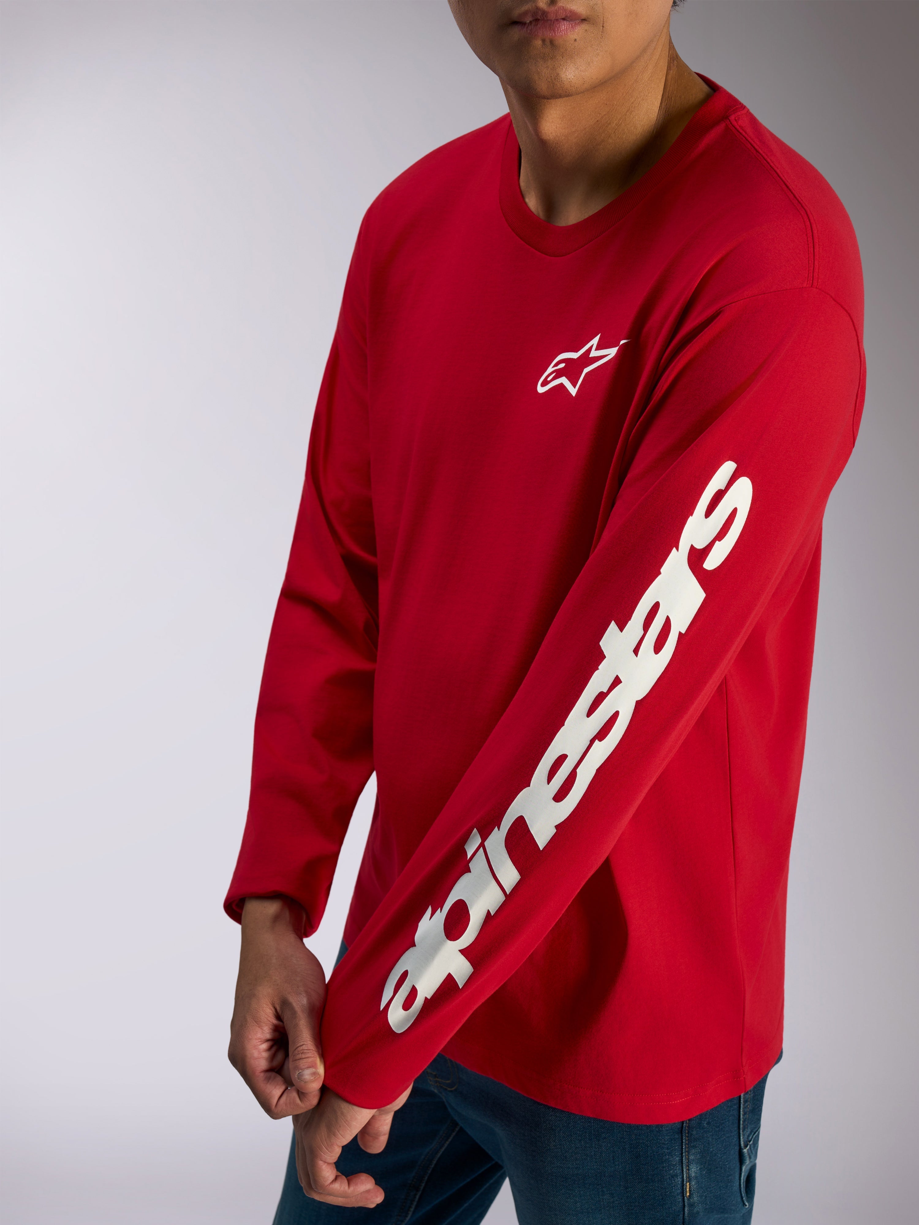 Alpinestars Trackside CSF Tee, t-shirt à manches longues, rouge, logo Alpinestars blanc sur la poitrine et lettrage imposant sur la manche, streetwear décontracté porté avec un jean bleu