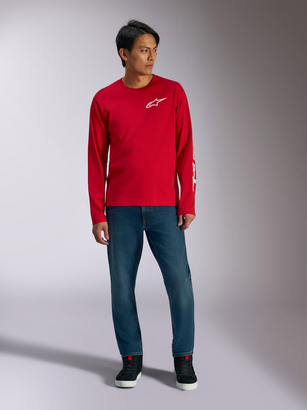 Alpinestars Trackside CSF Tee, t-shirt à manches longues, rouge avec logo Alpinestars blanc, photo lifestyle porté avec un jean bleu et des baskets noires, sportswear décontracté inspiré du sport automobile