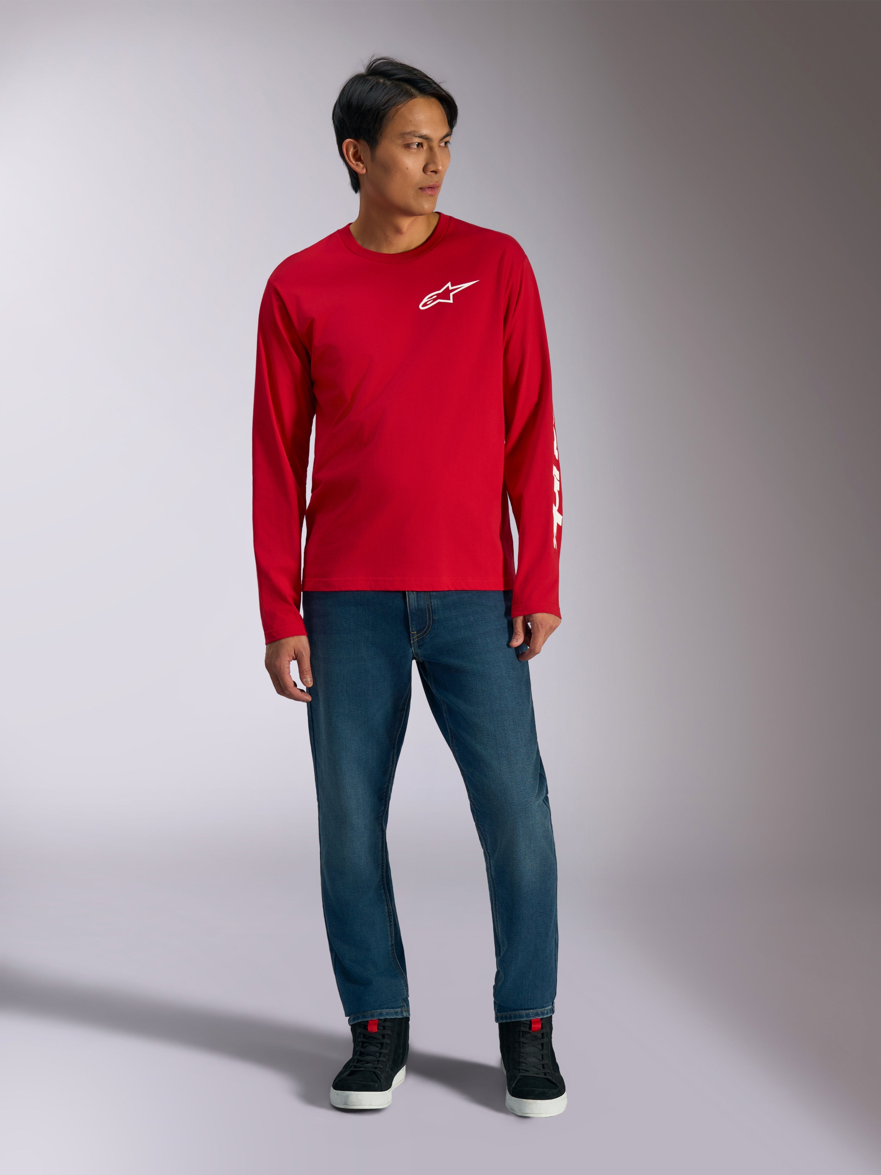 Alpinestars Trackside CSF Tee, t-shirt à manches longues, rouge avec logo Alpinestars blanc, photo lifestyle porté avec un jean bleu et des baskets noires, sportswear décontracté inspiré du sport automobile