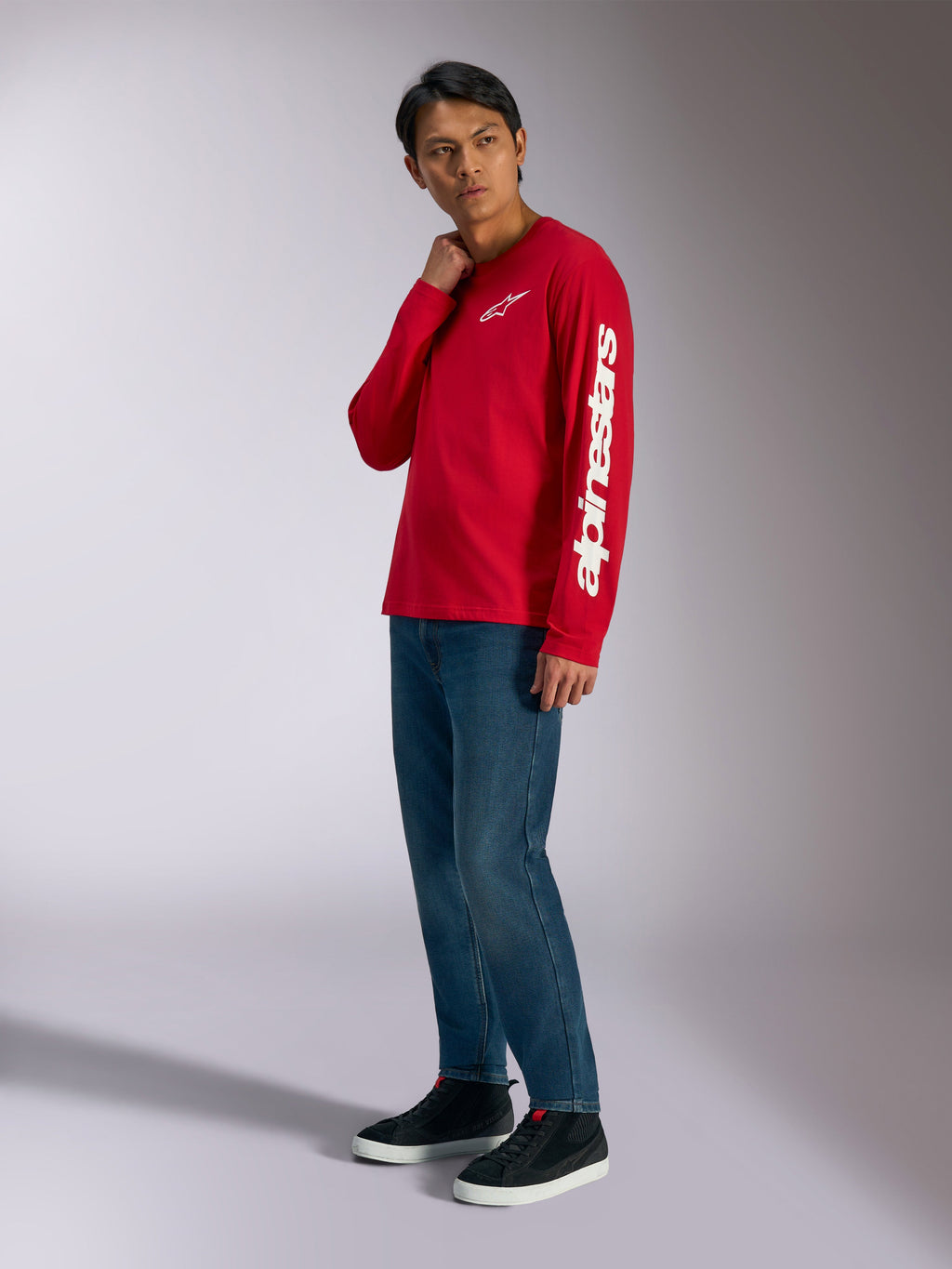 T-shirt à manches longues Alpinestars Trackside CSF, rouge avec logo Alpinestars blanc sur la poitrine et la manche, porté par un mannequin avec un jean bleu et des baskets noires, streetwear décontracté inspiré du sport automobile