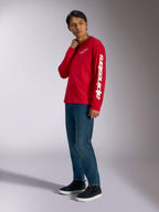 T-shirt à manches longues Alpinestars Trackside CSF, rouge avec logo Alpinestars blanc sur la poitrine et la manche, porté par un mannequin avec un jean bleu et des baskets noires, streetwear décontracté inspiré du sport automobile