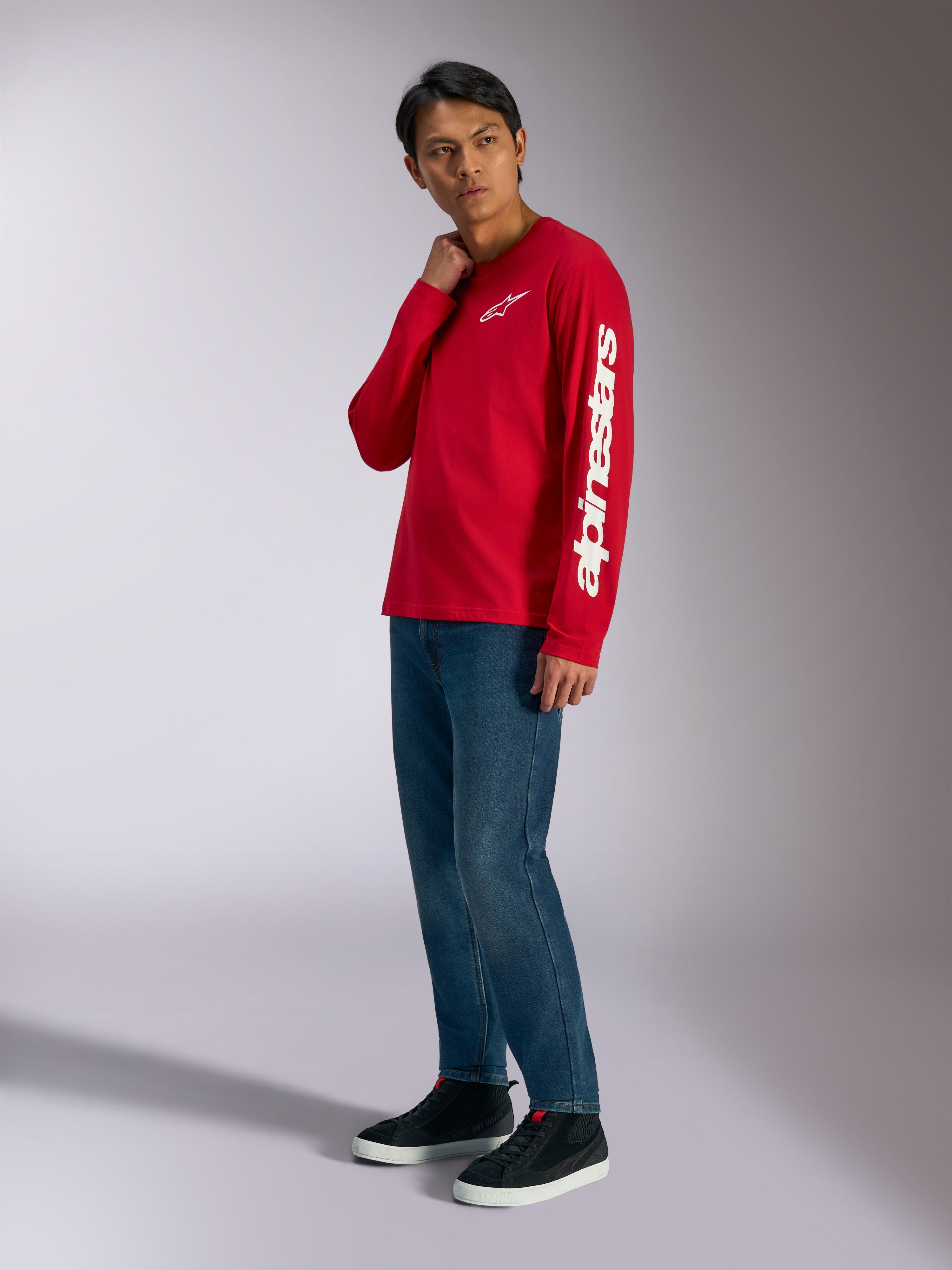 T-shirt à manches longues Alpinestars Trackside CSF, rouge avec logo Alpinestars blanc sur la poitrine et la manche, porté par un mannequin avec un jean bleu et des baskets noires, streetwear décontracté inspiré du sport automobile