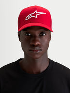 Alpinestars Casquette Snapback Ageless, casquette de sport rouge avec logo Astars brodé en blanc, visière incurvée et couronne structurée, portée par un modèle