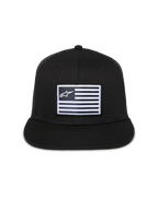 Casquette Trucker Flag Flat Alpinestars, noire, visière plate avec couronne structurée, écusson rectangulaire central avec drapeau blanc et logo Alpinestars, arrière en maille, streetwear décontracté inspiré du sport automobile