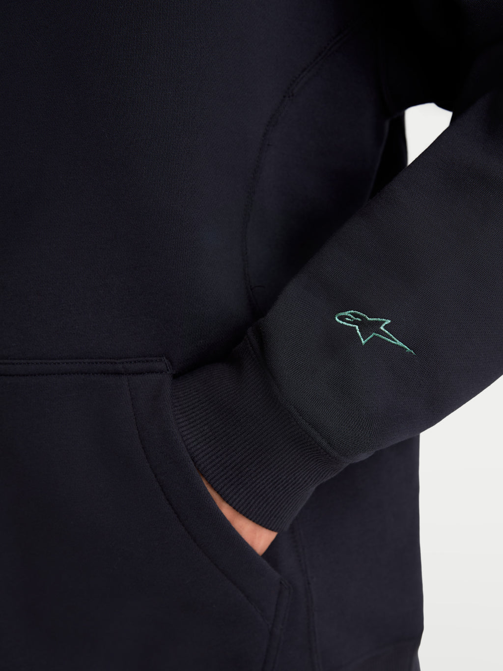 Alpinestars Guise Oversized Crew, Black Sportswear Fleece Pullover, detailed view showing the sleeve with a teal embroidered Astars logo, ribbed cuff, and kangaroo pocket entry, premium cotton and recycled polyester blend sweatshirt.