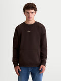 Alpinestars Guise Oversize Sweat, pull en polaire marron de style sportswear, coupe mixte décontractée sur modèle, coton et polyester recyclé, avec poche kangourou et logos Alpinestars brodés sur la poitrine et la manche.