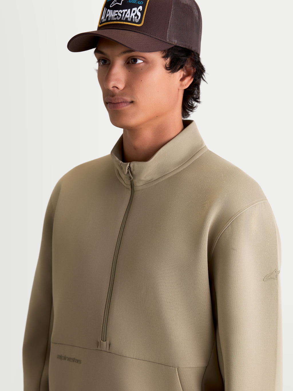Alpinestars sweatshirt demi-zip Apera, pull sportswear beige putty pour homme, avec fermeture demi-zip et poche kangourou, logos ton sur ton, style décontracté inspiré du sport automobile porté par un modèle.
